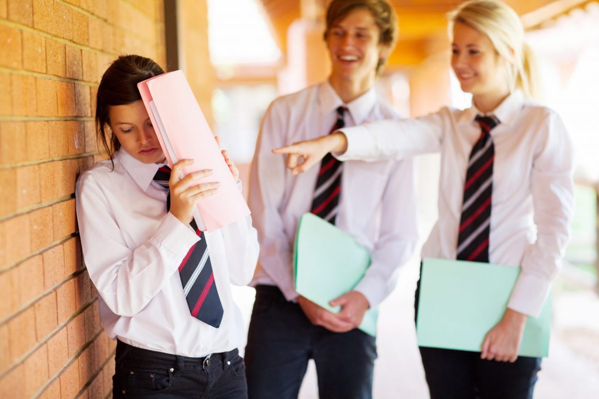 two students bullying another student hiding behind a folder